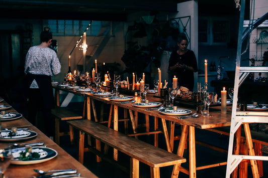 Anonymous women serving wooden tables with plates and glassware among burning candles while preparing for banquet in modern p