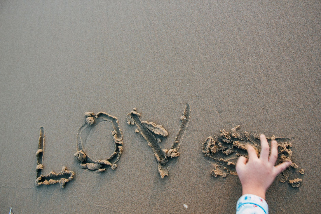 A child's hand writing 'love' in the sand at the beach, creating a heartfelt message.