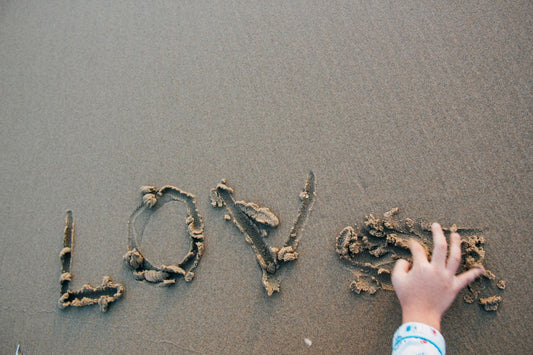 A child's hand writing 'love' in the sand at the beach, creating a heartfelt message.