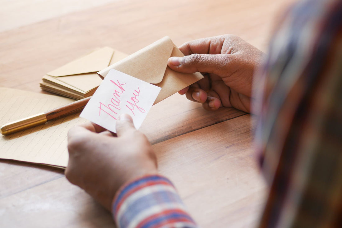 Close-up of hands holding a thank you note in an envelope on a table.